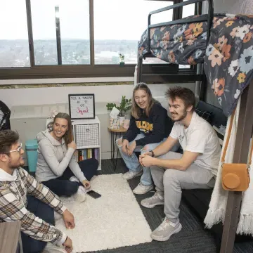 four students in a residence hall room chatting 