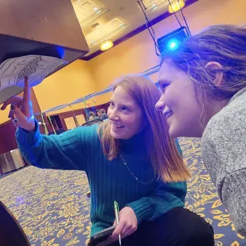 two students look for a scavenger hunt clue under a table